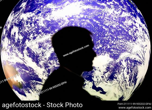 11 November 2021, United Kingdom, Glasgow: A man sits in front of a glowing globe at the UN Climate Change Conference COP26