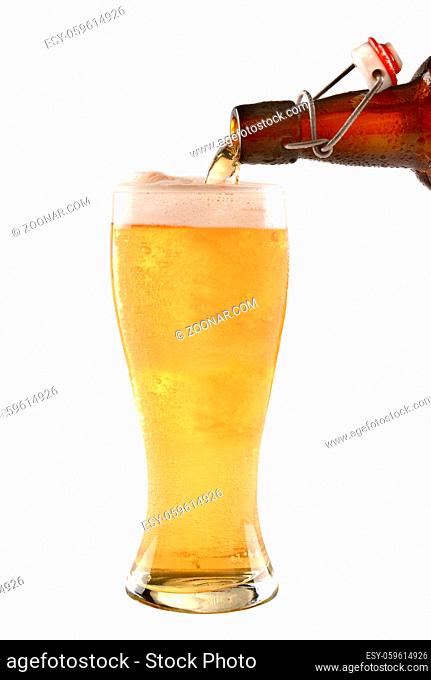 A brown swing top bottle of beer pouring into a glass on white