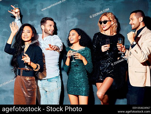 Diverse group of young people dancing in night club, enjoy party and have fun. Young friends drinking champagne and hanging out at night club