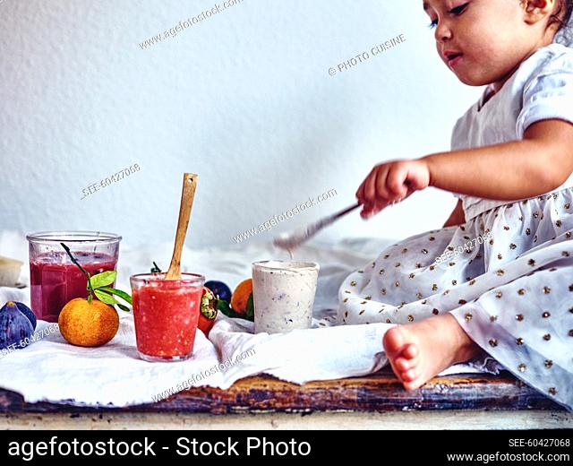Little girl tasting fruit smooties on a table