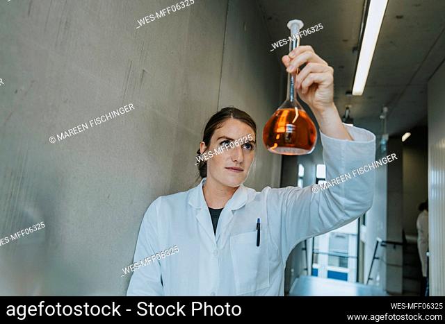 Scientist holding liquid solution while standing at clinic corridor