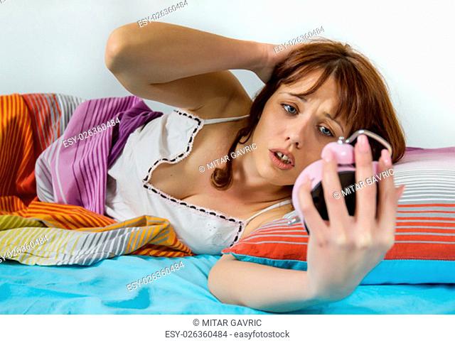 Oversleeping woman in panic, late waking up, looking on the alarm clock