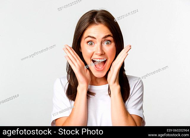 Close-up of excited happy brunette girl looking amazed, holding hands near face astonished