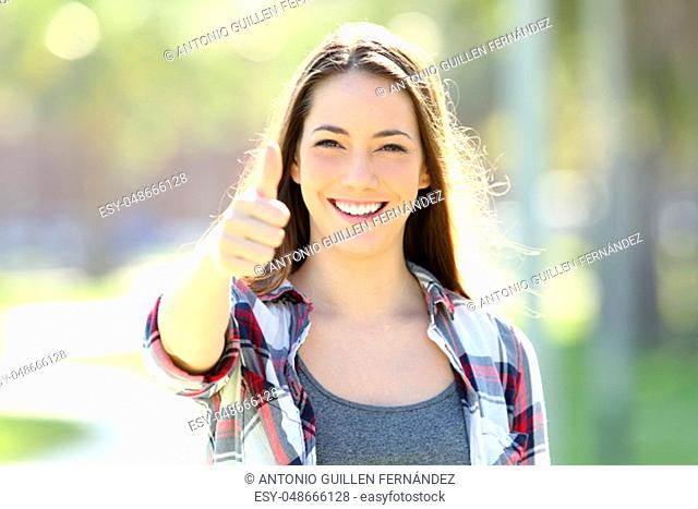 Front view of a happy girl gesturing thumbs up and looking at you alone in the street