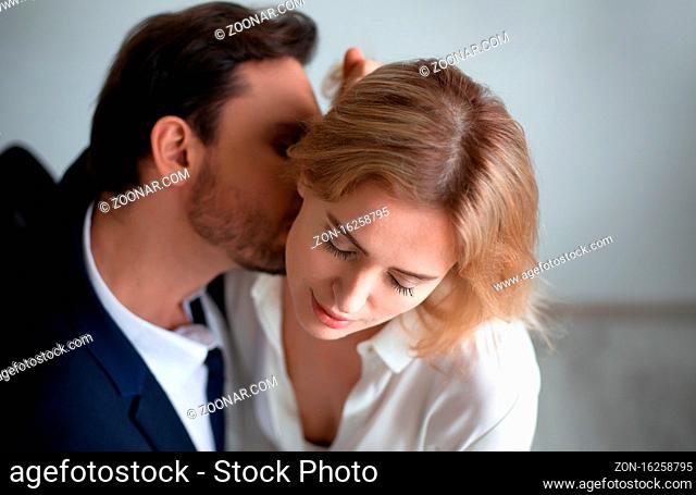 Business man kissing neck of young blonde woman closed eyes. Passion kiss. Enjoyment or workplace romance concept