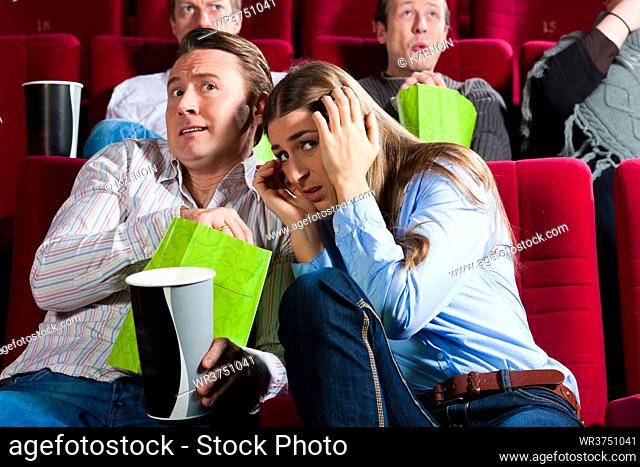 Couple in cinema watching a movie; it seems to be a horror movie