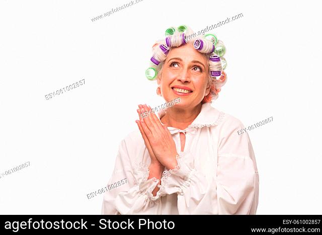 Happy grandmother posing in studio over white background with her hands clasped. Toothy smiling beautiful elderly lady looking away