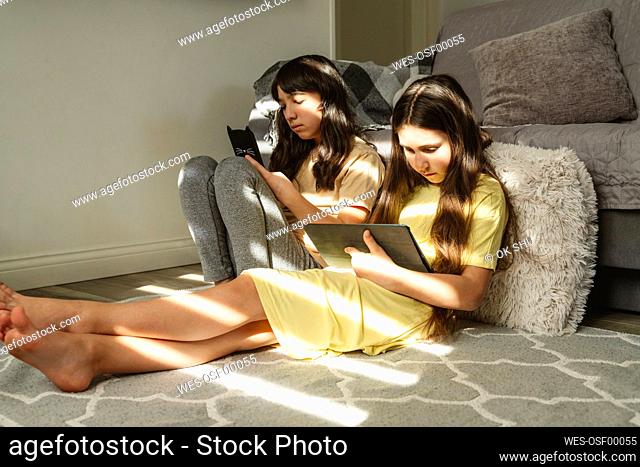 Female friends using gadgets in living room at home