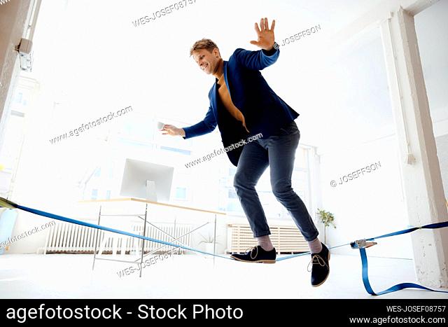 Happy businessman balancing on tightrope in office