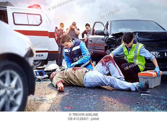 Rescue workers tending to bloody car accident victim in road