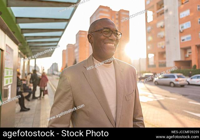 Happy businessman with eyeglasses at tram station in city