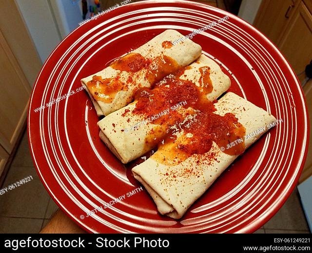 burritos on red plate with spicy salsa and chili powder in kitchen