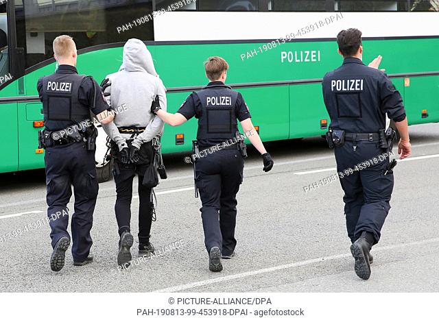13 August 2019, Lower Saxony, Wolfsburg: Police have taken an activist into custody while clearing a blockade of a car train, and handcuffed him to a police bus