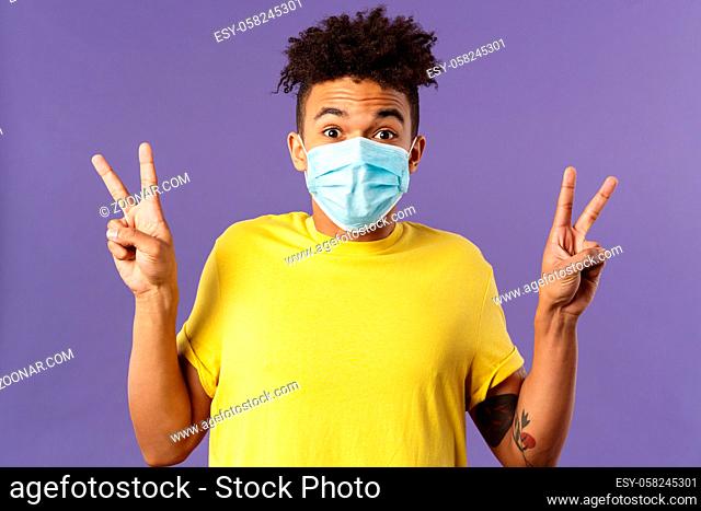 Medicine, covid19, coronavirus and people concept. Upbeat, hispanic man with afro haircut, wear medical face mask and show peace signs, staying positive