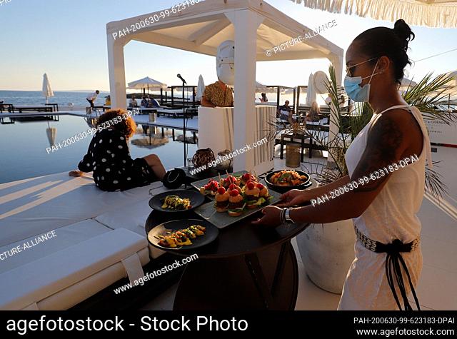 23 June 2020, Spain, Palma: A waitress with a face mask serves the customers of the Bar Purobeach in Cala Estancia on the beach Playa de Palma