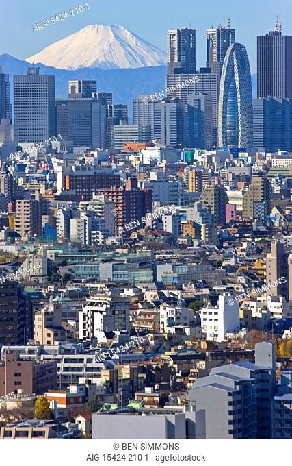 A telephoto view on a clear winter day captures a snow-capped Mt. Fuji rising dramatically beyond the skyscrapers, including Tokyo City Hall