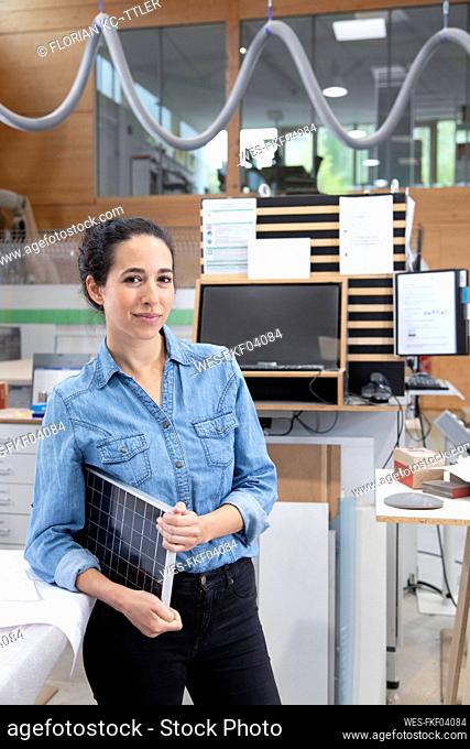 Female entrepreneur with solar panel model standing in factory