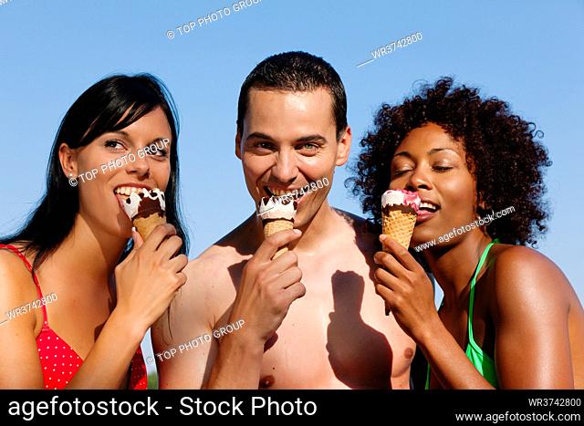 Group of friends - one man and two women eating ice cream in swimwear and bikini, it seems to be a hot summer day