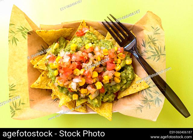 Top view of delicious Mexican nachos served with cheese and guacamole mixed with vegetables against green background