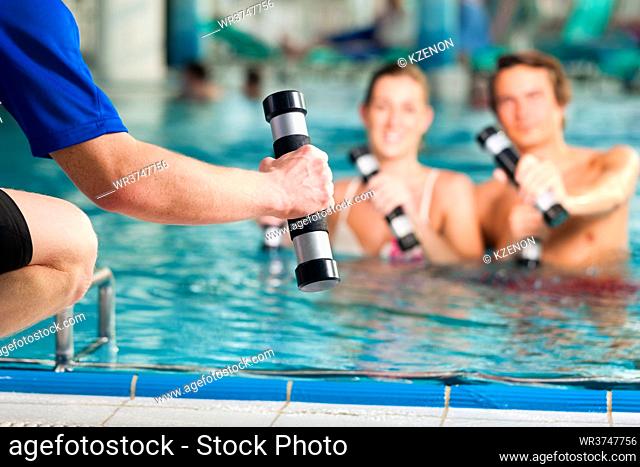 Fitness - a young couple (man and woman) doing sports and gymnastics or water aerobics under water in swimming pool or spa with dumbbells and instructor