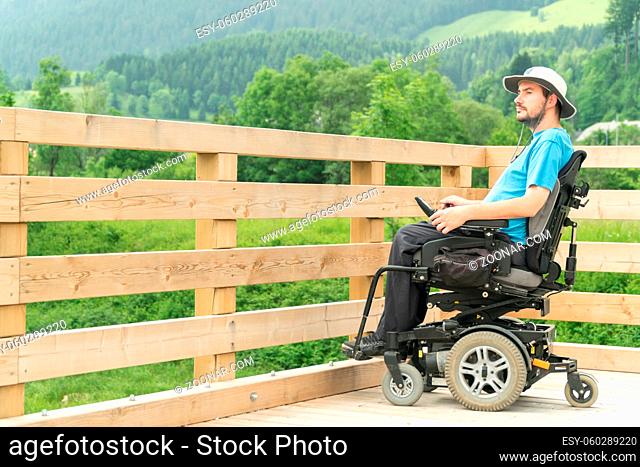 Photo of disabled Young man in electric wheelchair on a boardwalk enjoying his freedom and observing nature