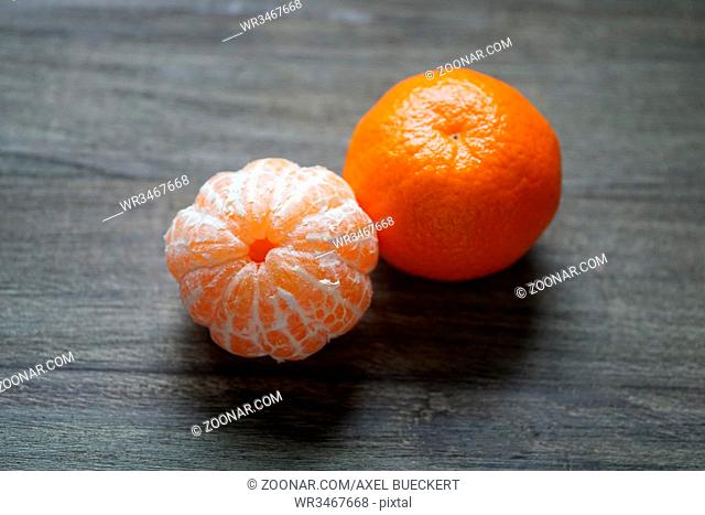 peeled and unpeeled clementines or tangerines or mandarin oranges on rustic wooden background with selective focus