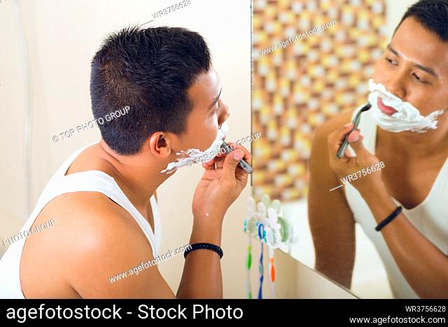 Asian man shaving in front of bathroom mirror