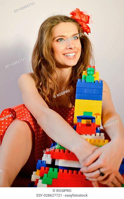 portrait of beautiful funny young pinup girl with great dental whitening teeth smile in red polka dot dress having fun playing with toy constructor and looking...