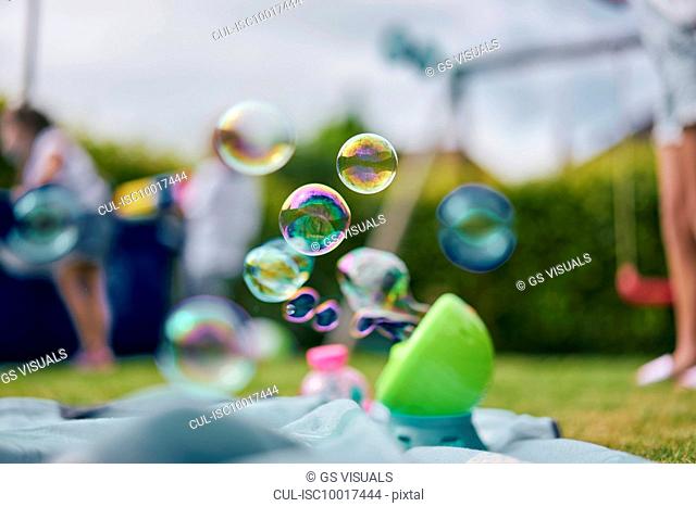Soap bubble machine, family playing in garden in background
