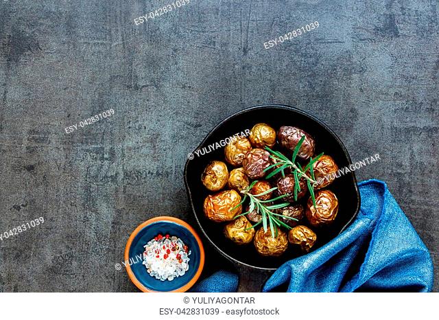 Homemade fried baby potatoes in vintage cast iron pan on black concrete background, copy space. Healthy food concept. Overhead shot