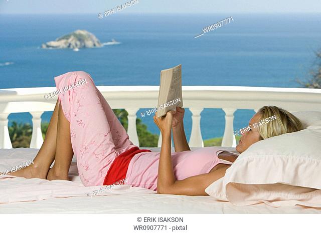 Woman relaxing and reading on balcony overlooking ocean