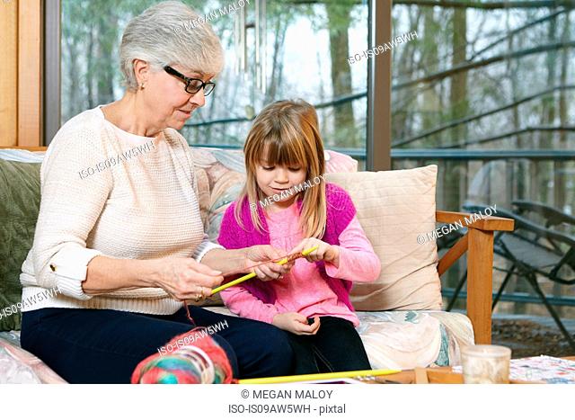 Senior woman teaching granddaughter knitting on living room sofa