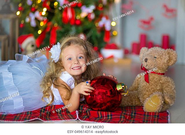 Young beautiful girl in blue white elegant evening dress sitting on floor near christmas tree and presents on a new year eve Interior with christmas decorations