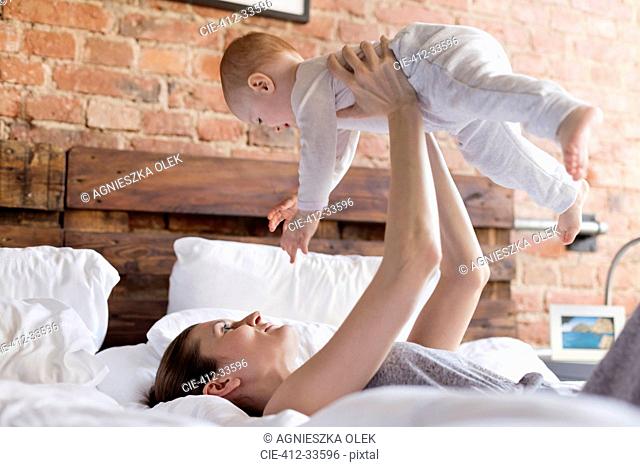 Mother lifting baby daughter overhead on bed