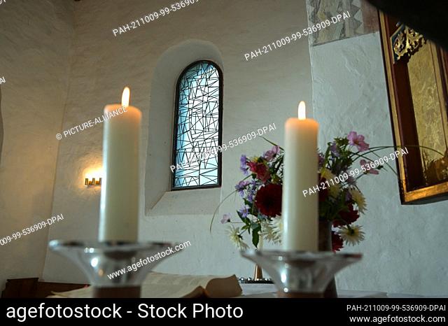 09 October 2021, Saxony-Anhalt, Altjeßnitz: Candles burn in front of one of the modern church windows designed by the artist B