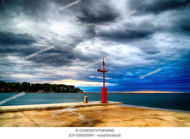 Sunset on pier on the Mediterranean sea with red steel lookout and white lighthouse in the cloudy background near Porec in Croatia