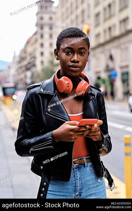 Woman wearing jacket and headphones using mobile phone while standing in city
