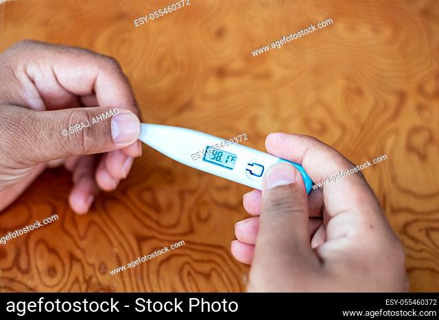 Man holding digital thermometer with temperature reading in Fahrenheit