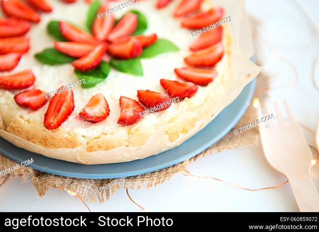 Very beautiful summer cheesecake decorated with strawberries - stands on a white wooden table, close-up
