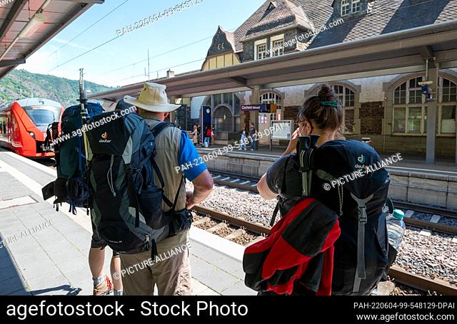 04 June 2022, Rhineland-Palatinate, Cochem: Tourists with hiking equipment wait on the platform of Cochem station for the approaching regional train