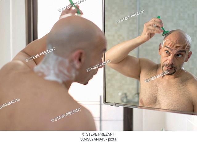Over the shoulder view of mature man shaving his head in bathroom