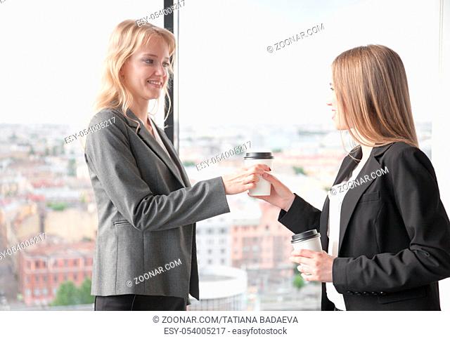 Business woman offering coffee to colleague in office with panoramic windows with view at city