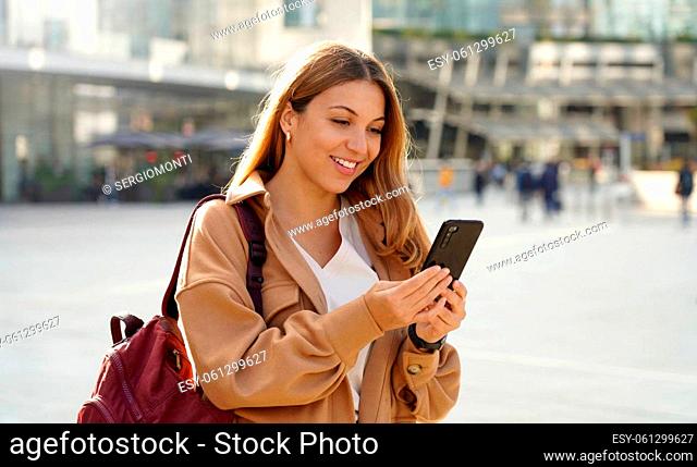 Pretty student girl watching excited her smartphone in city street