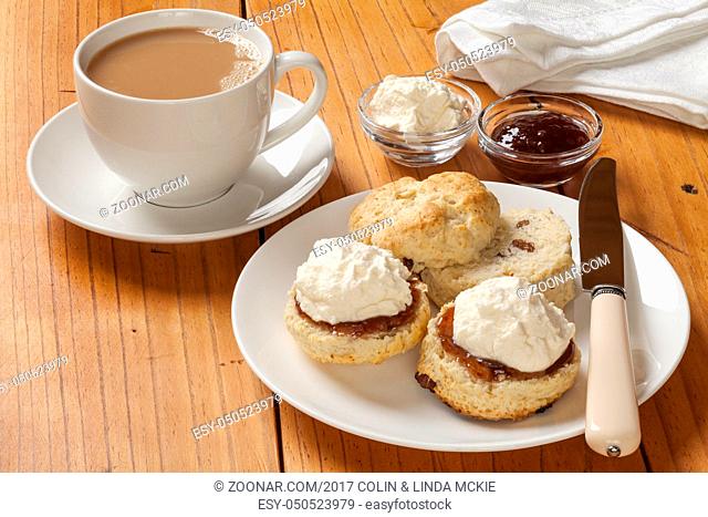 Devon cream tea, scones, jam, cream and a cup of tea, on an old pine table