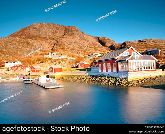 Traditional fishing village. Cottages at the coast on the rocky island. Red white building shinning in spring warm sun rays
