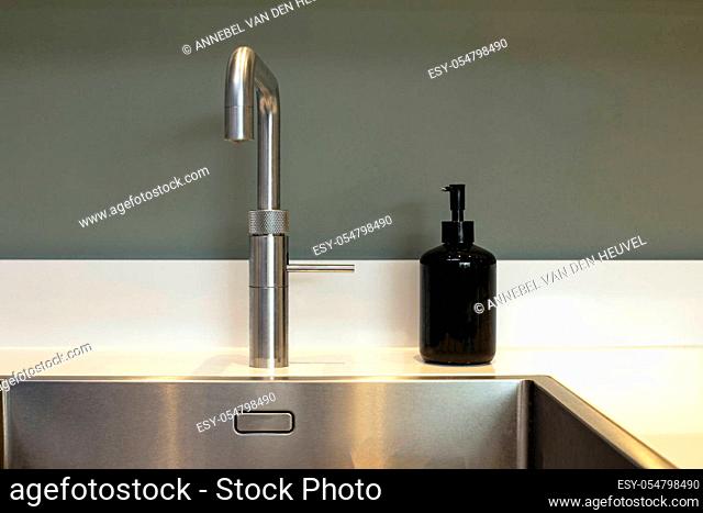 Empty clean kitchen sink and soap dispenser modern design with grey wall close-up