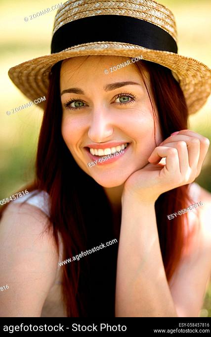 Portrait of young foxy lady in garden. Close up view of beautiful woman in straw hat, holding her hand close to chin