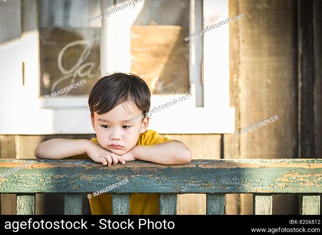 Melancholy mixed-race boy leaning on porch railing