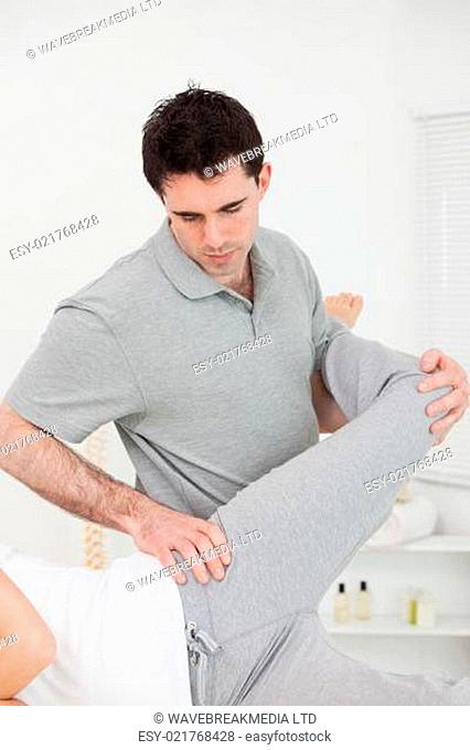 Physiotherapist standing behind a woman while stretching her leg in a room
