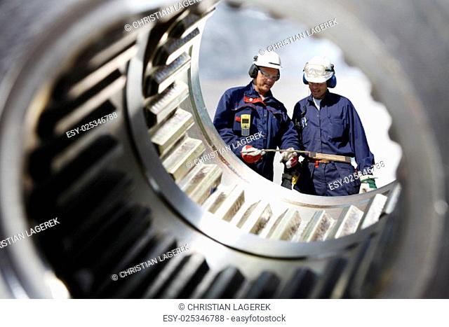 two mechanics, engineers seen through a large cogwheels axle